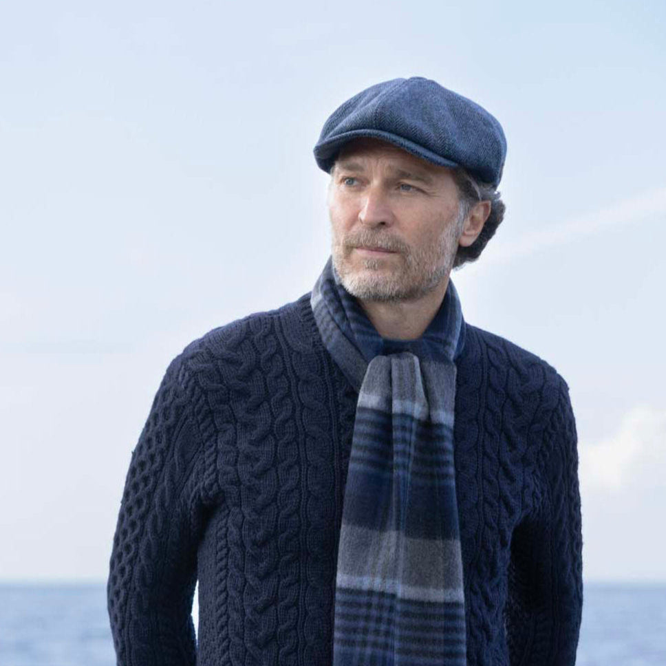 Man wearing a navy sweater, cap, and plaid scarf against a light blue background