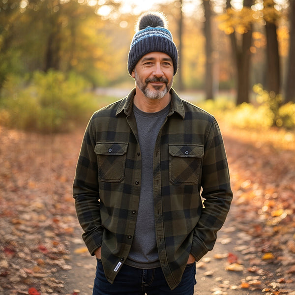 Man wearing a navy blue fairisle beanie hat standing in a park with autumn leaves and trees in the background
