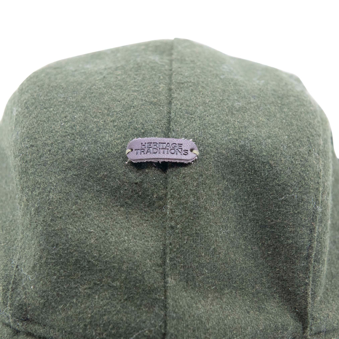 Close-up of an olive green felt cap with a small purple metal brand patch reading &