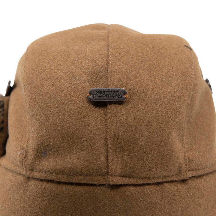 Close-up of the crown of a brown wool winter cap with a small black metal brand plaque reading &