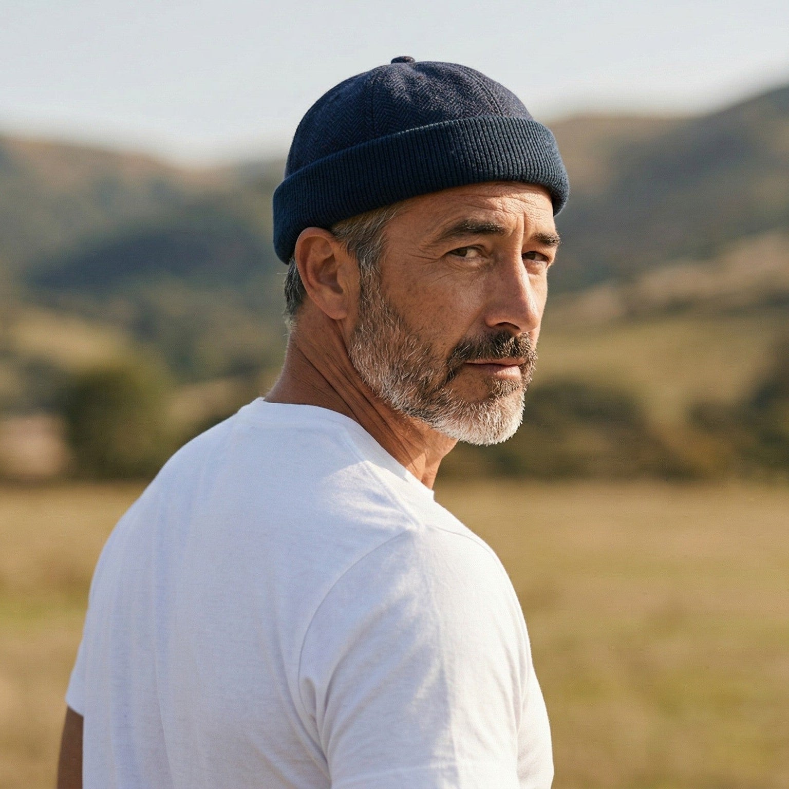 Man wearing a navy cap and white shirt standing in a field with blurred background
