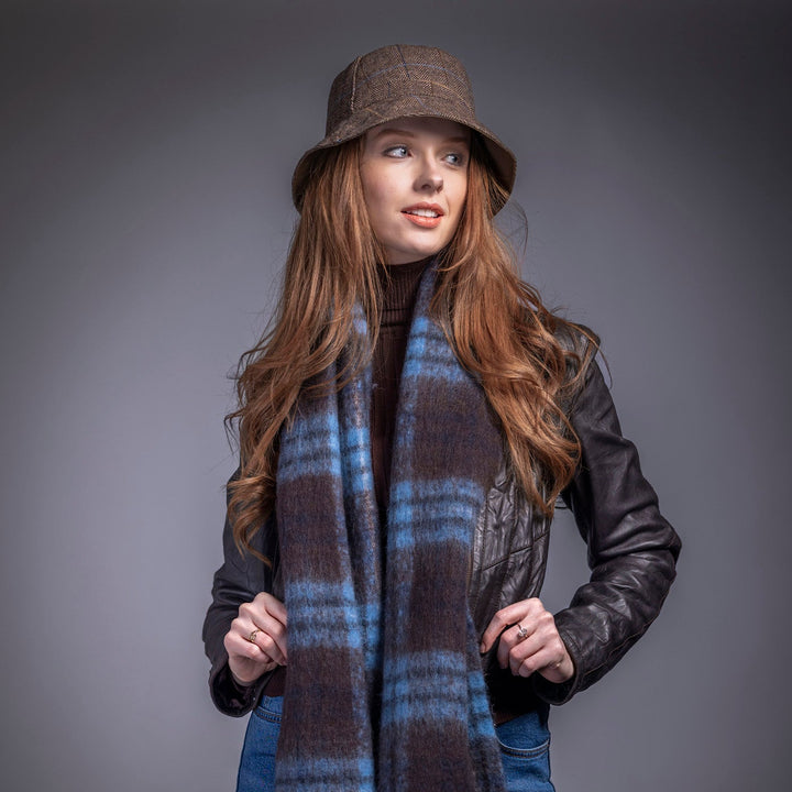 Woman wearing a plaid scarf, leather jacket, and hat against a gray background