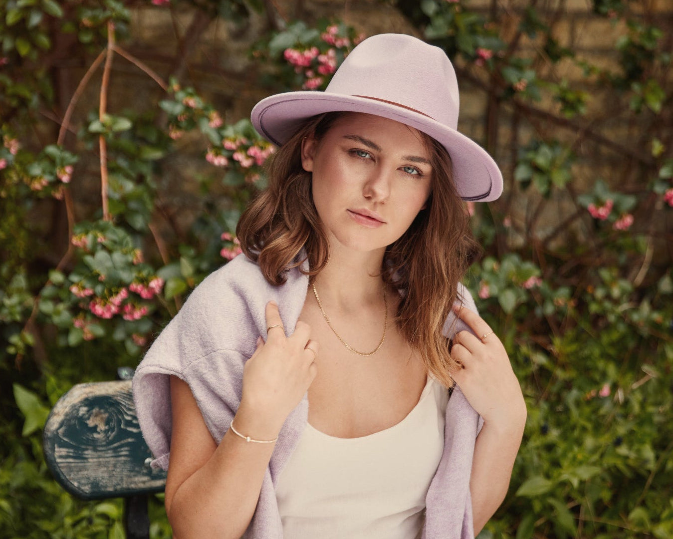 Woman wearing a pink hat and light purple shawl in a garden setting