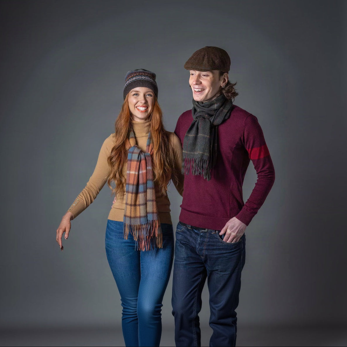 Two people wearing scarves and hats against a gray background