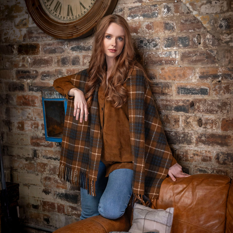 Woman wearing a plaid poncho sitting on a leather couch against a brick wall.