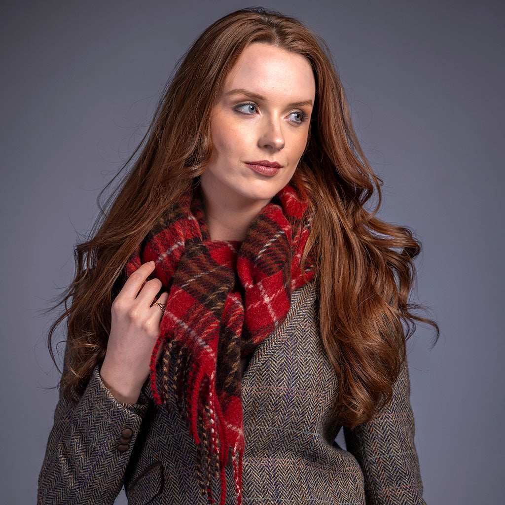 Woman wearing a red plaid scarf and brown coat against a gray background