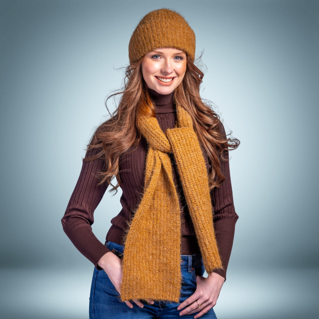 Woman wearing a mustard yellow knit hat and scarf against a gray background