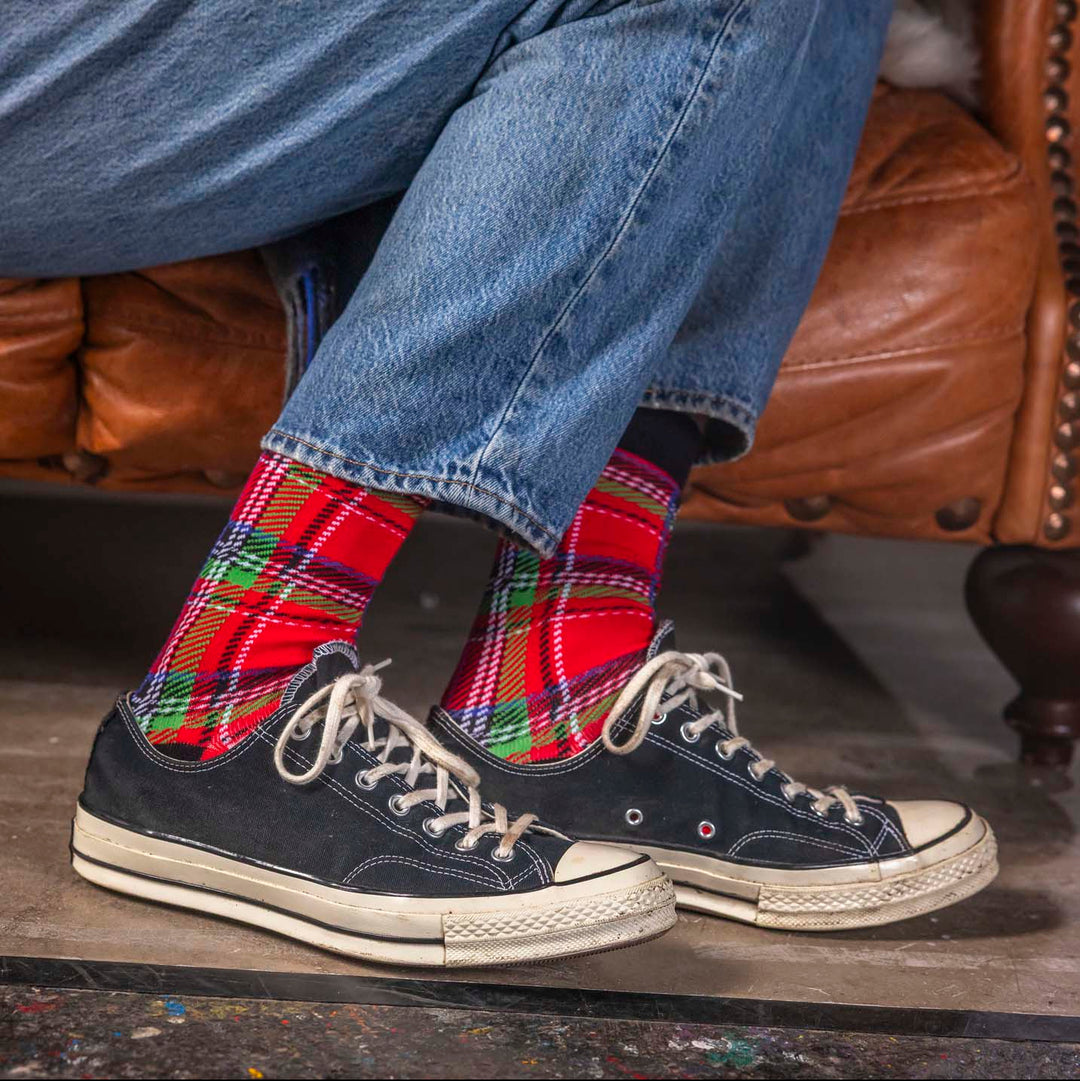 Person wearing plaid socks and navy sneakers sitting on a brown leather couch.