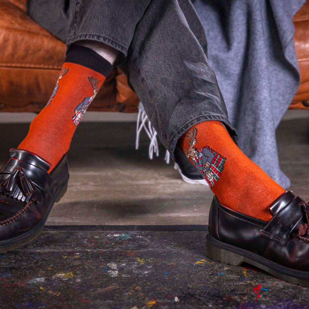Person wearing orange socks with tattoos and black loafers on a dark floor.