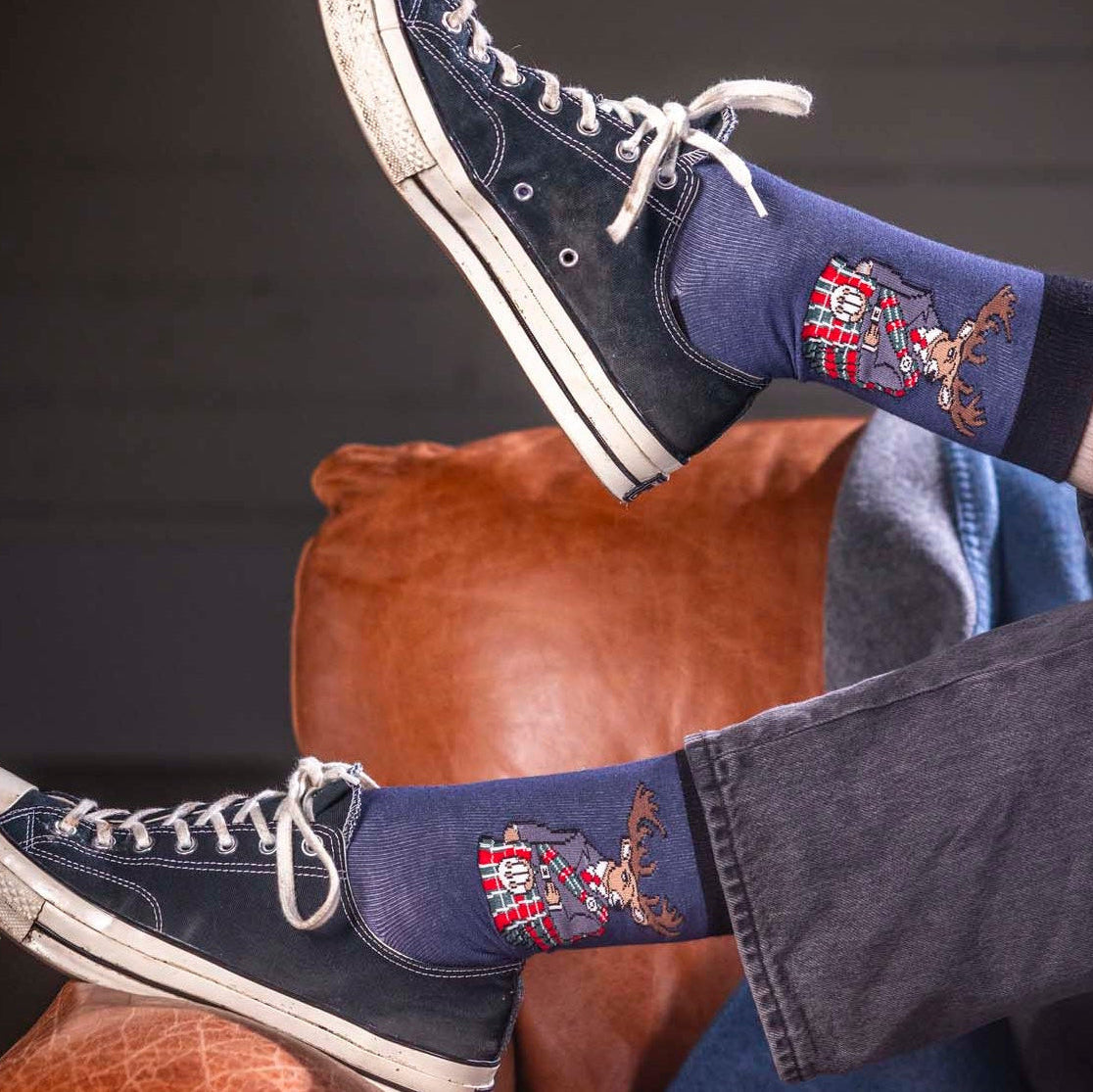 Person wearing navy blue sneakers with plaid patterned socks, sitting on a brown leather chair.