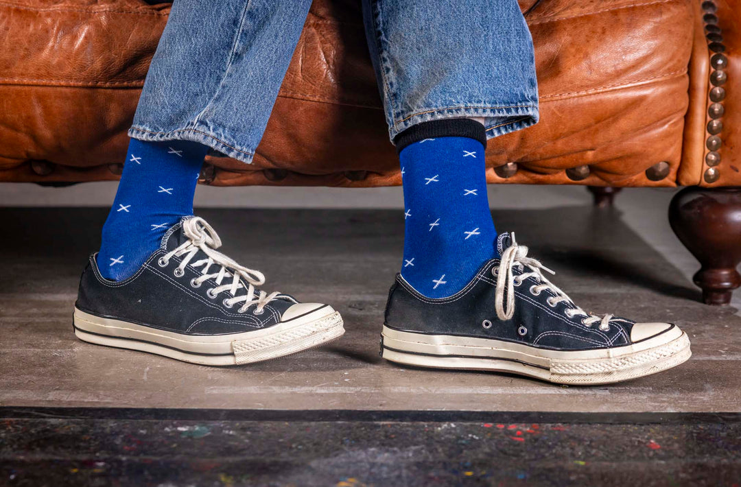Person wearing blue socks with Scotland flag pattern and black sneakers on a wooden floor.