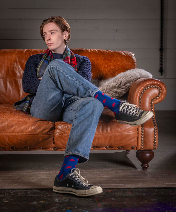 Person sitting on a brown leather couch wearing blue jeans, a dark sweater, and colorful socks.